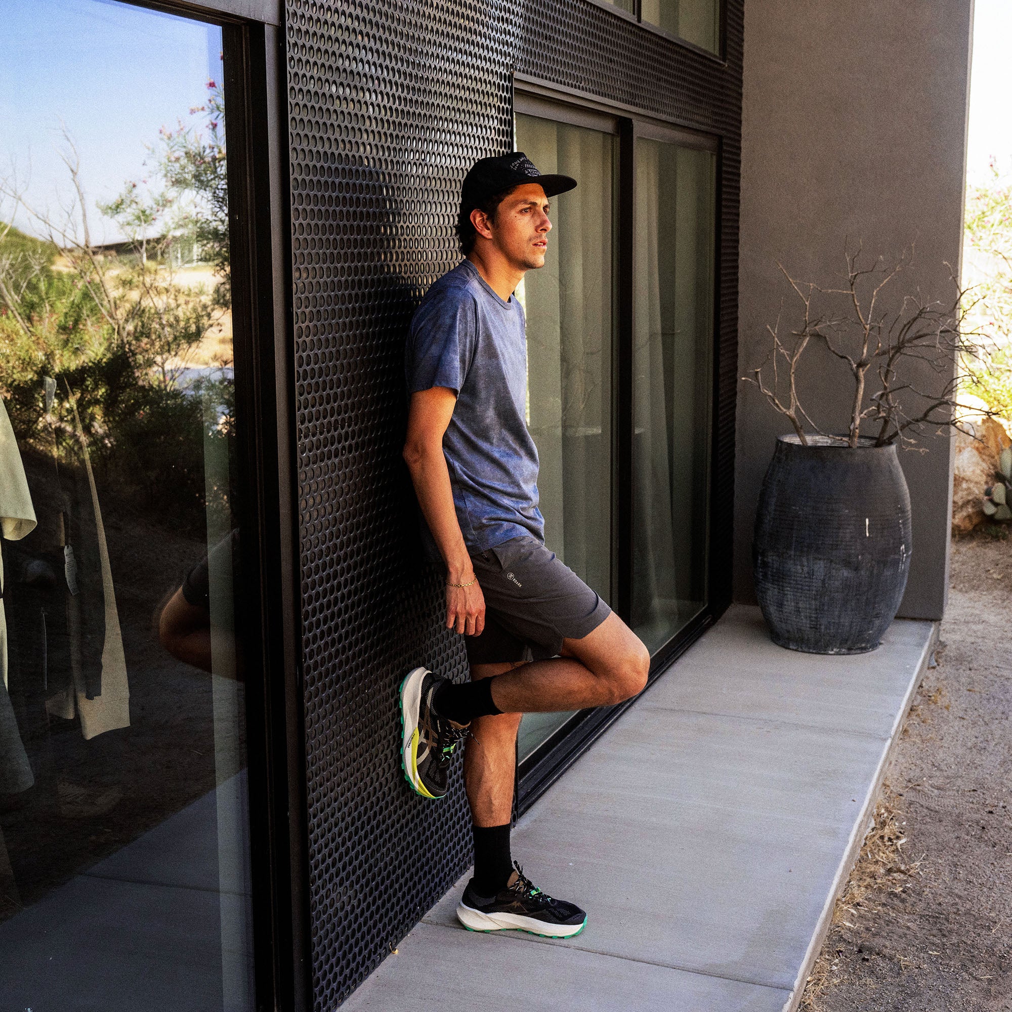 Man wearing navy blue short-sleeve tee and black shorts stretching against modern building exterior