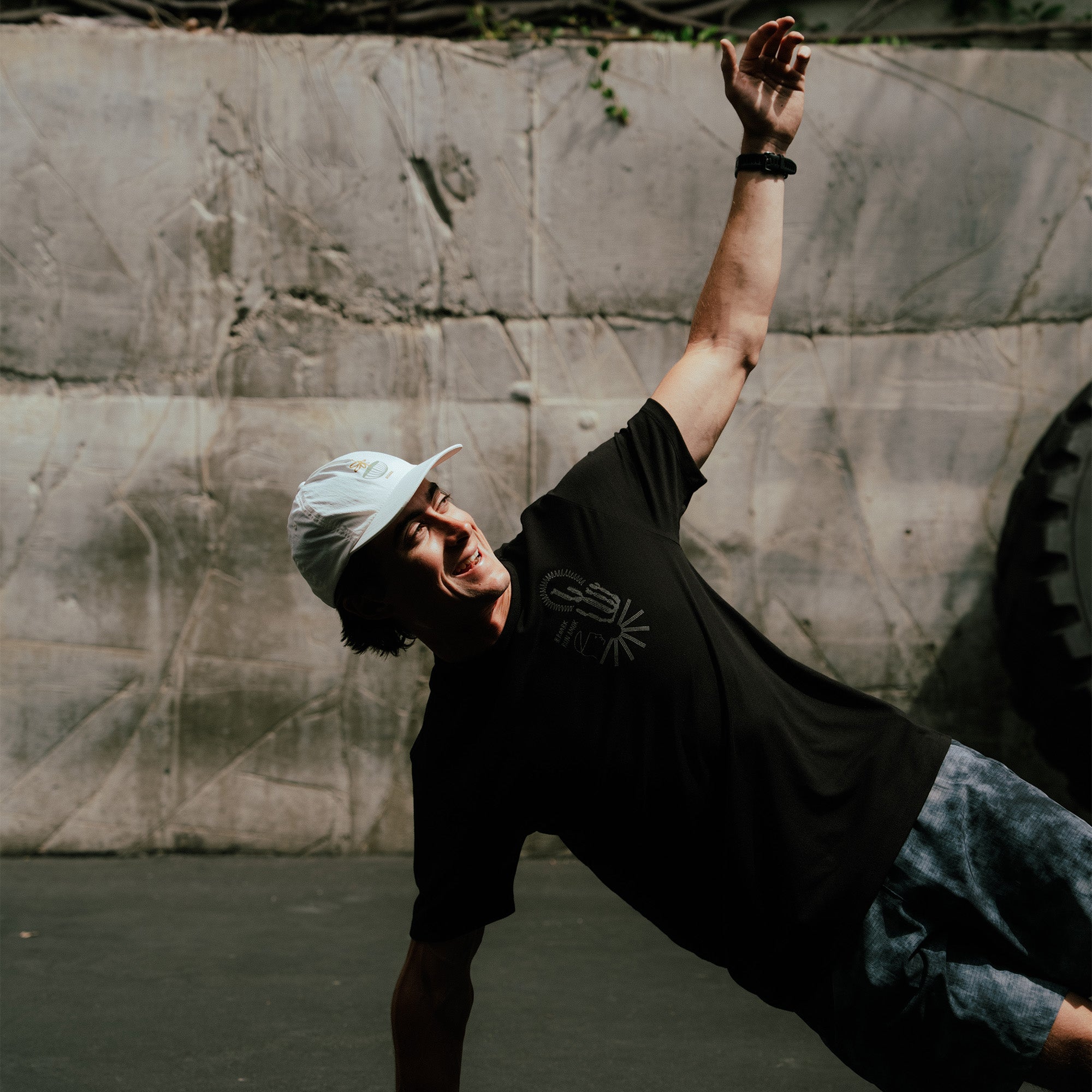 Person wearing black short-sleeve tee and blue cap with fist raised against concrete wall backdrop