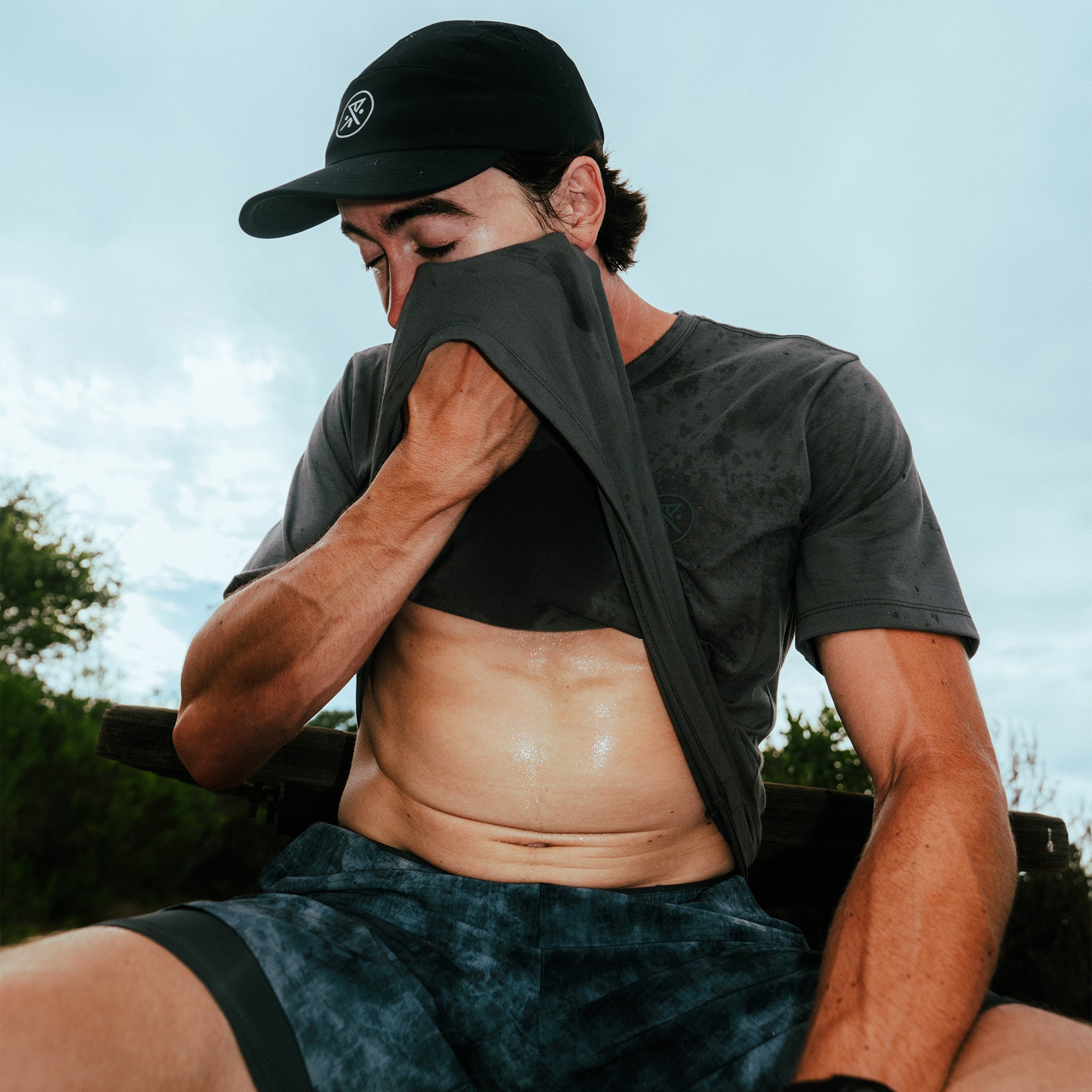 Black Mathis Active short sleeve tee worn by man outdoors, shown pulled up to display fit and fabric detail against sky background