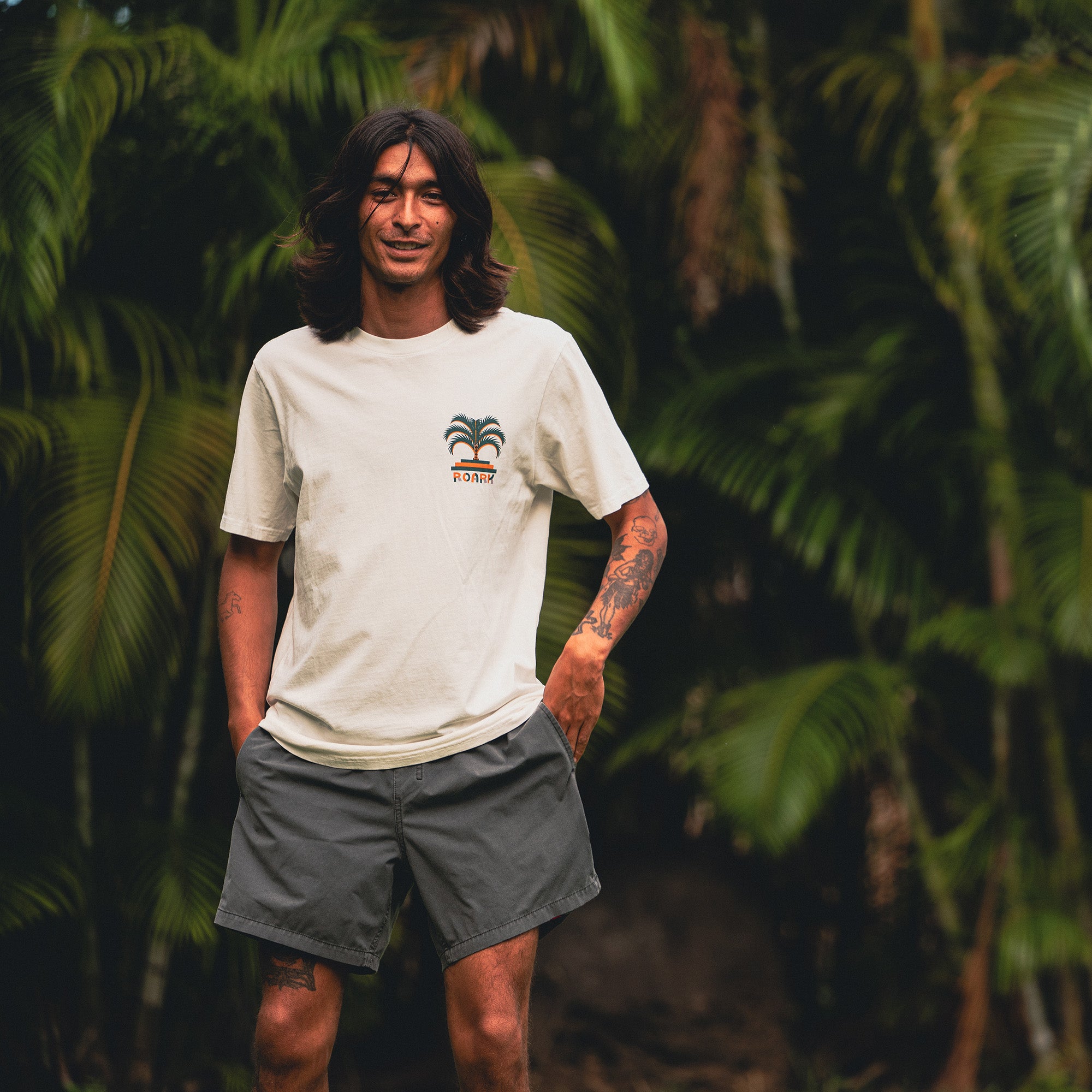Model wearing Roark's adventure-inspired Moto Palm Premium Tee paired with stylish boardshorts, perfect for an active outdoor lifestyle.