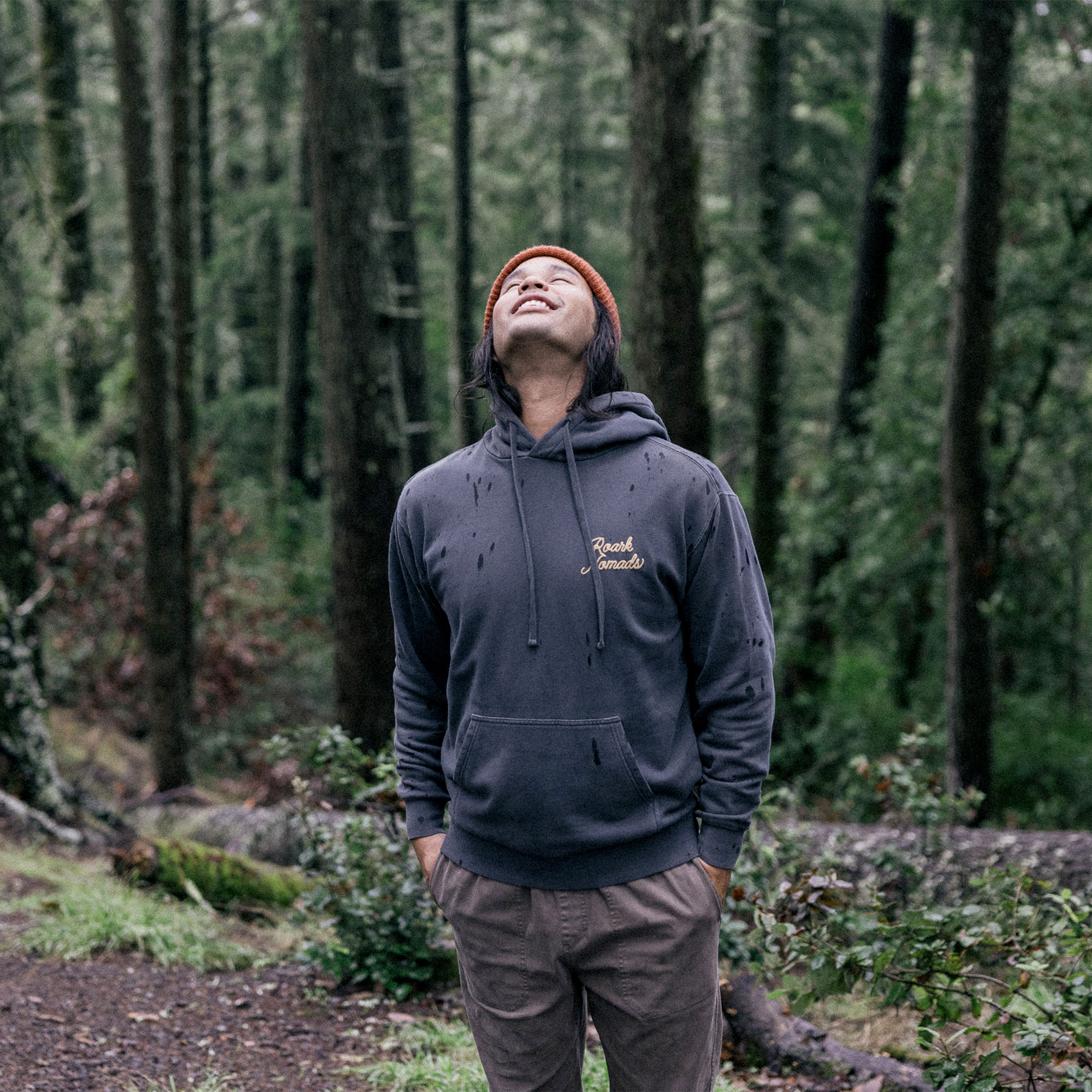 Person wearing Roark Nomads Badge fleece hoodie exploring a lush forest setting, emphasizing adventure and connection with nature.