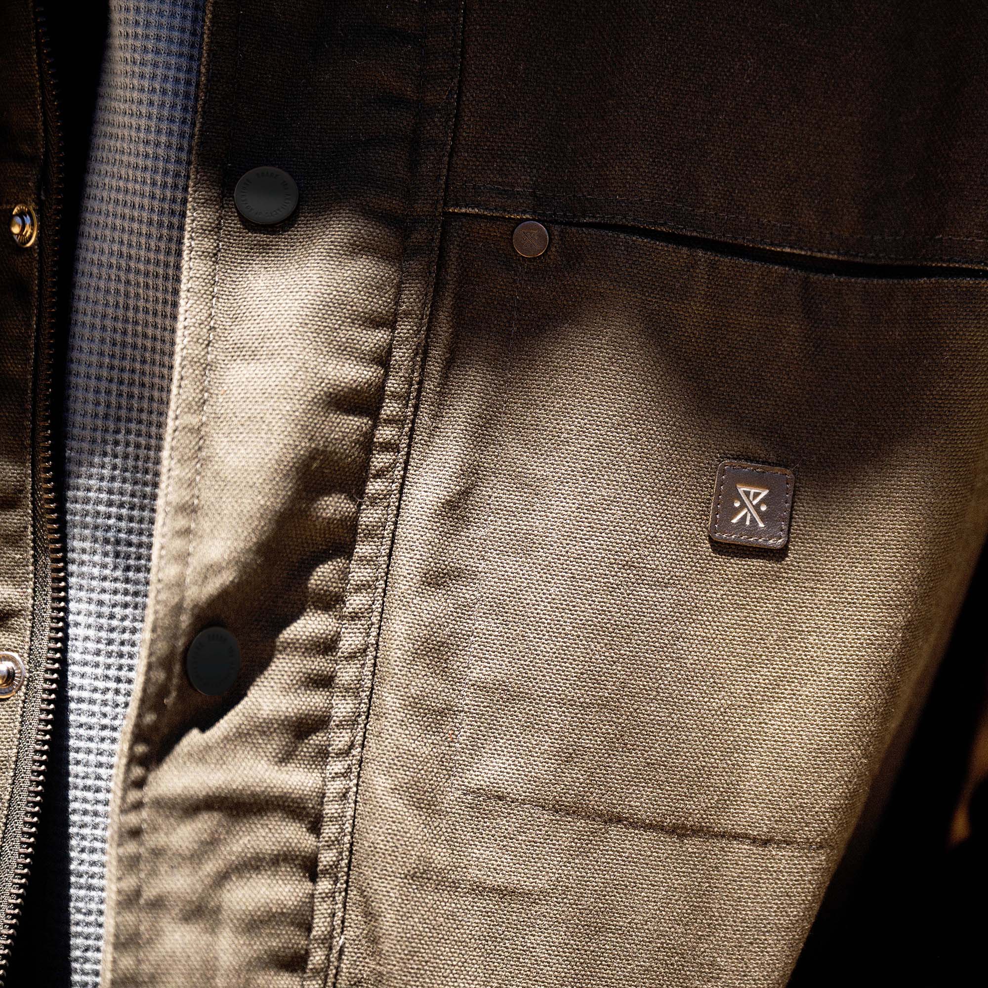 Waxed canvas jacket interior showing tan lining with black buttons and branded leather patch label visible