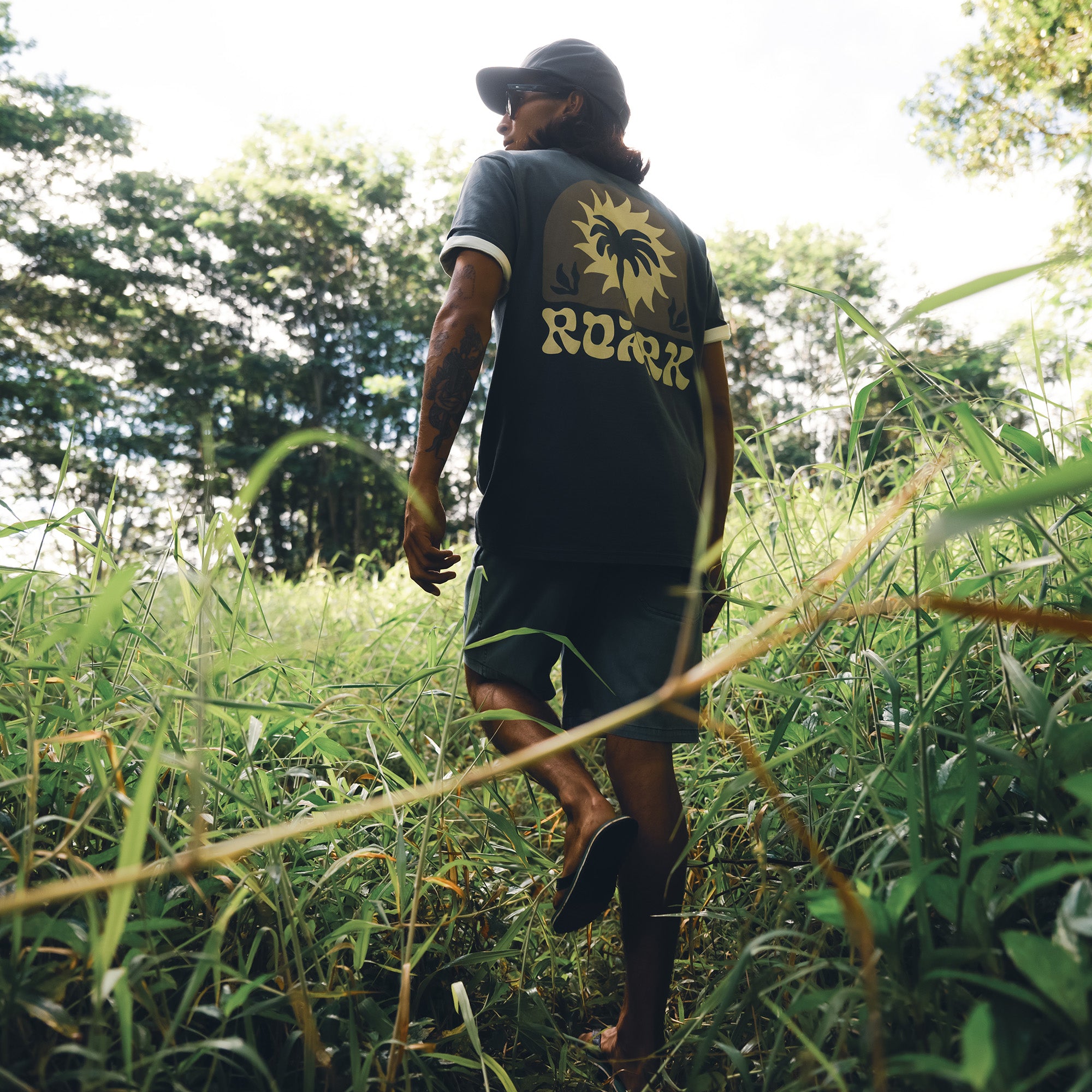 Model wearing Roark's Palm Premium Tee with a baseball cap, embodying the adventurous spirit in an active outdoor setting.