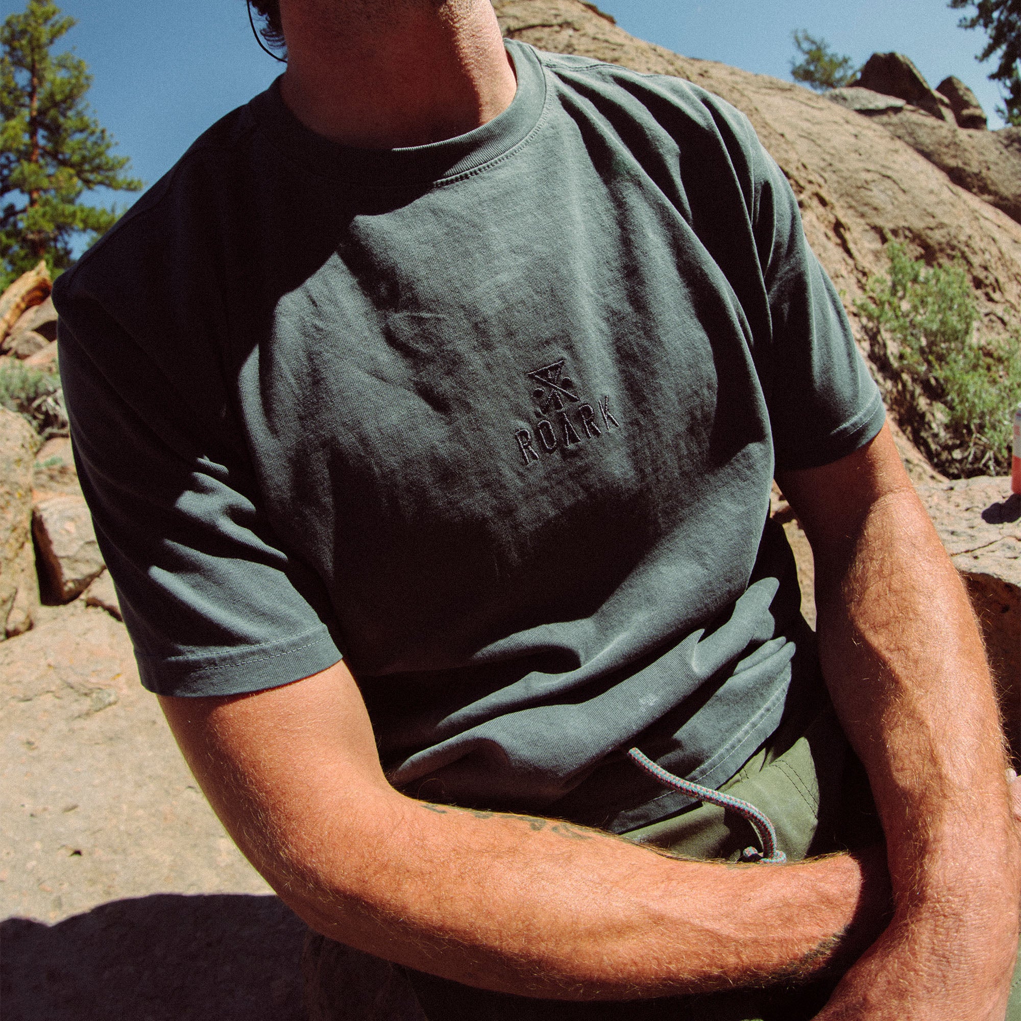 Person standing in active pose wearing the Safe Camp Embroidery Tee from Roark, featuring unique embroidery, styled with headgear for an adventurous look.