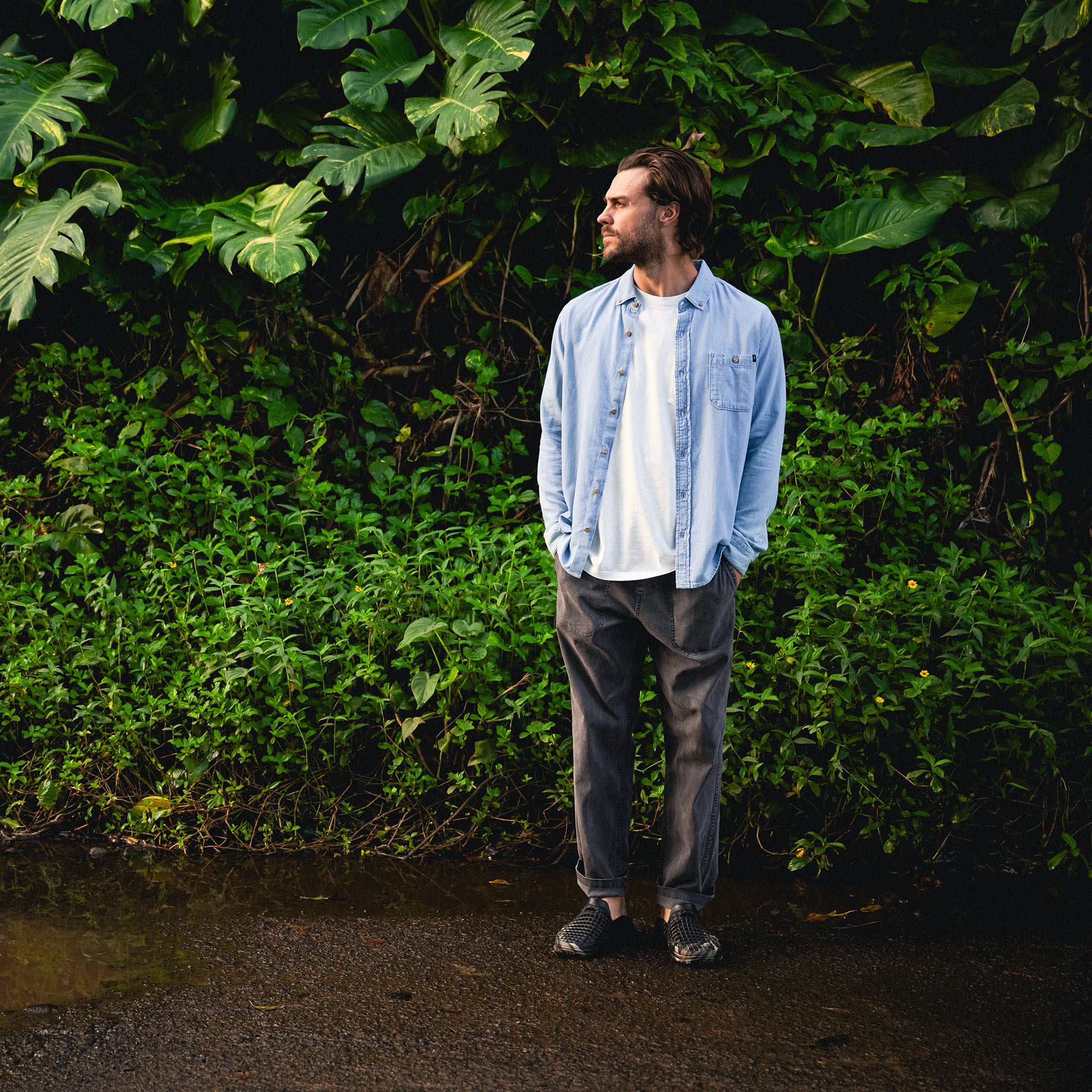 Man standing in nature wearing a Scholar Chambray button-up shirt, featuring long sleeves made of denim in a stylish grey color.
