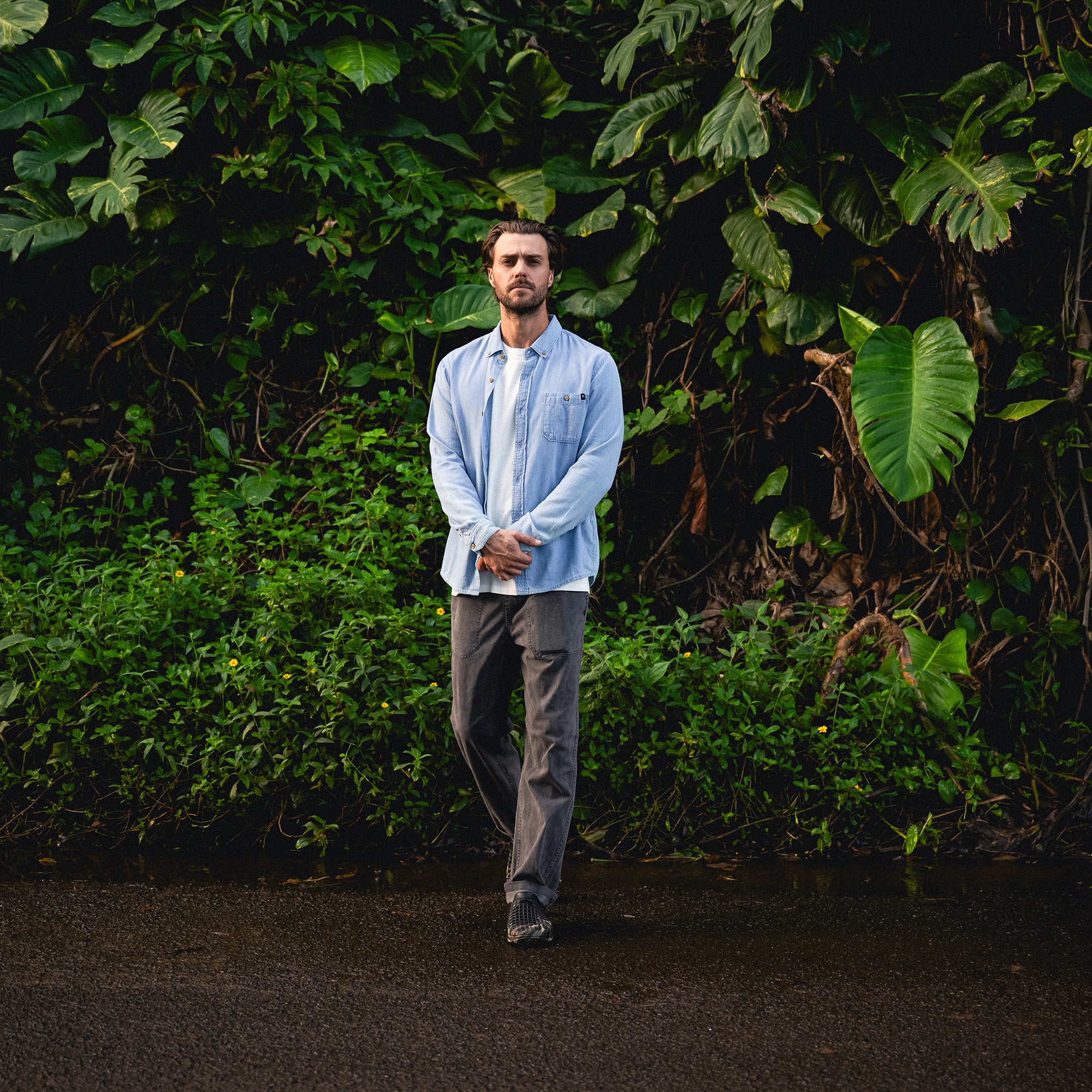 Man standing in a Scholar Chambray button-up denim shirt, featuring long sleeves and a structured collar, perfect for outdoor adventures and travel.