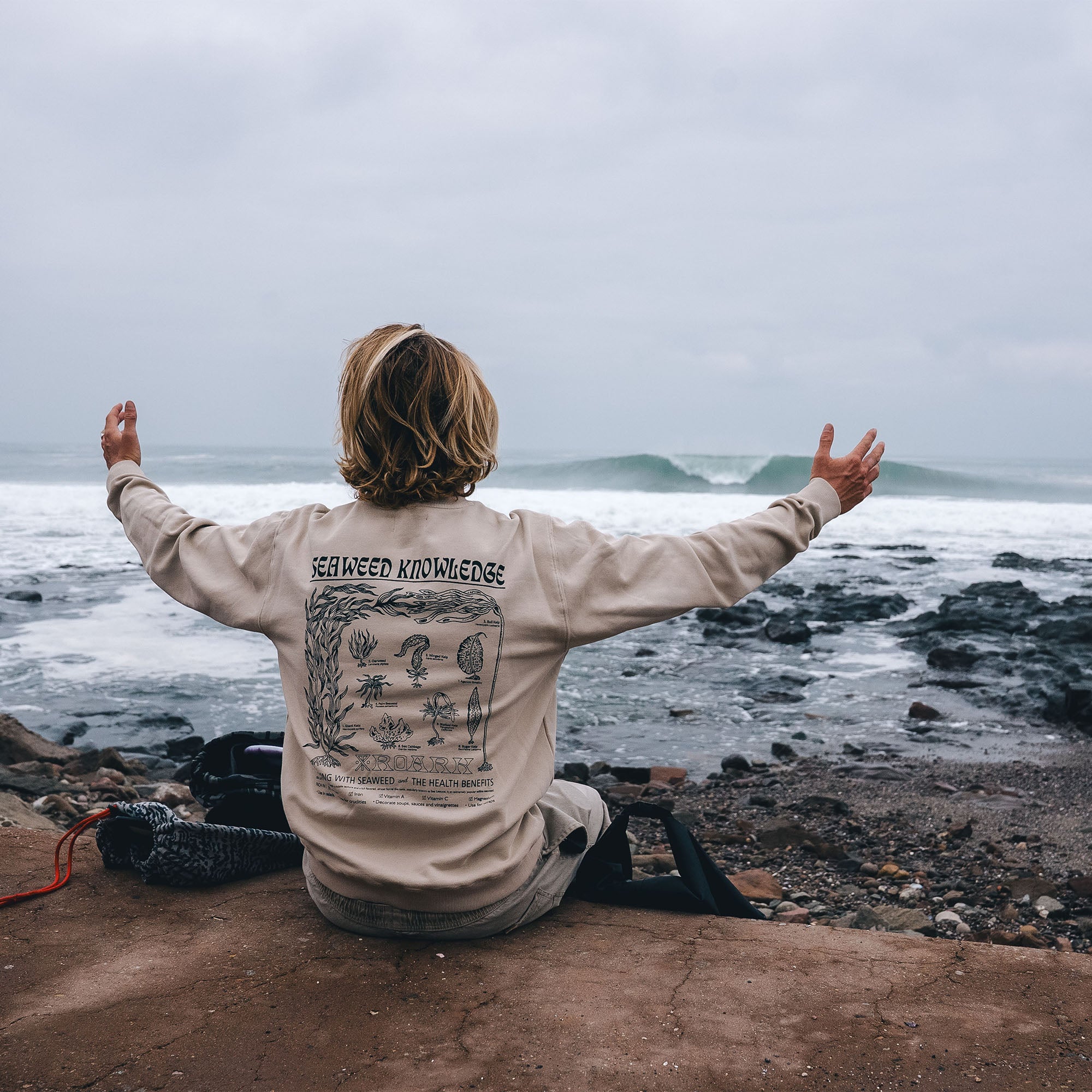 Group of friends wearing Roark seaweed knowledge fleece tees, enjoying a coastal adventure on a sandy beach