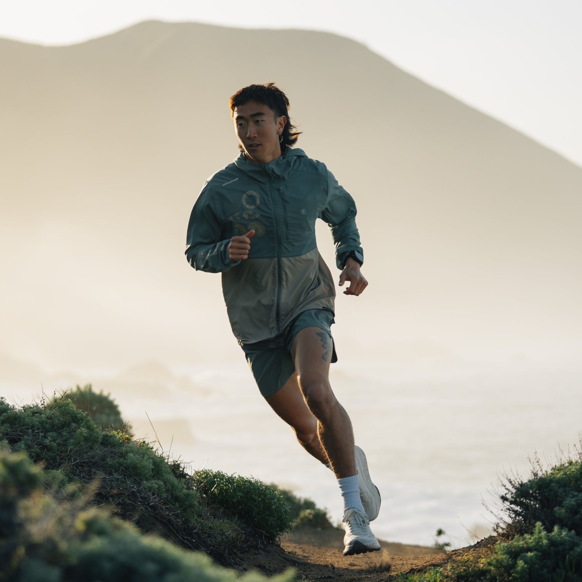 Person jogging in a scenic outdoor setting wearing a Secondwind 3.0 Jacket, perfect for outdoor recreation and exercise