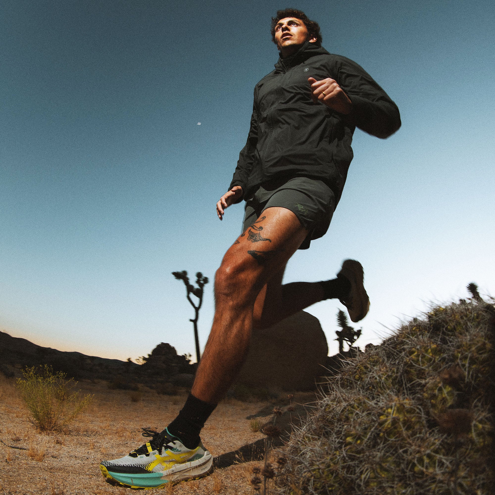 Man wearing black Shield Rain Jacket jogging on desert trail with clear blue sky in background