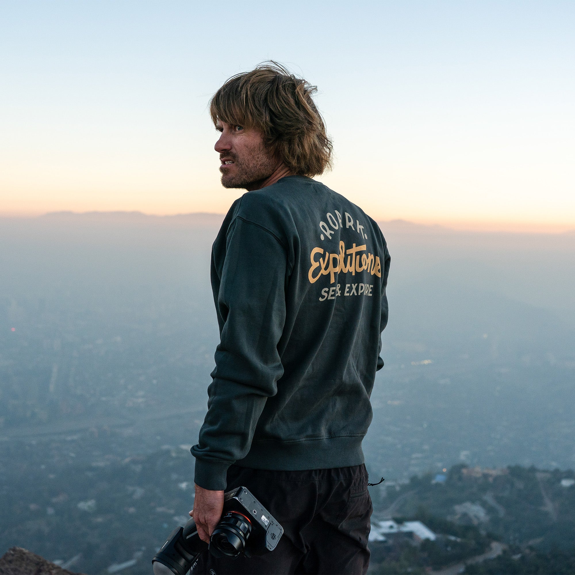 Bearded man in a Sign Writer Fleece jacket with denim sleeves, standing by palm trees in a winter setting, blending urban and adventure style.