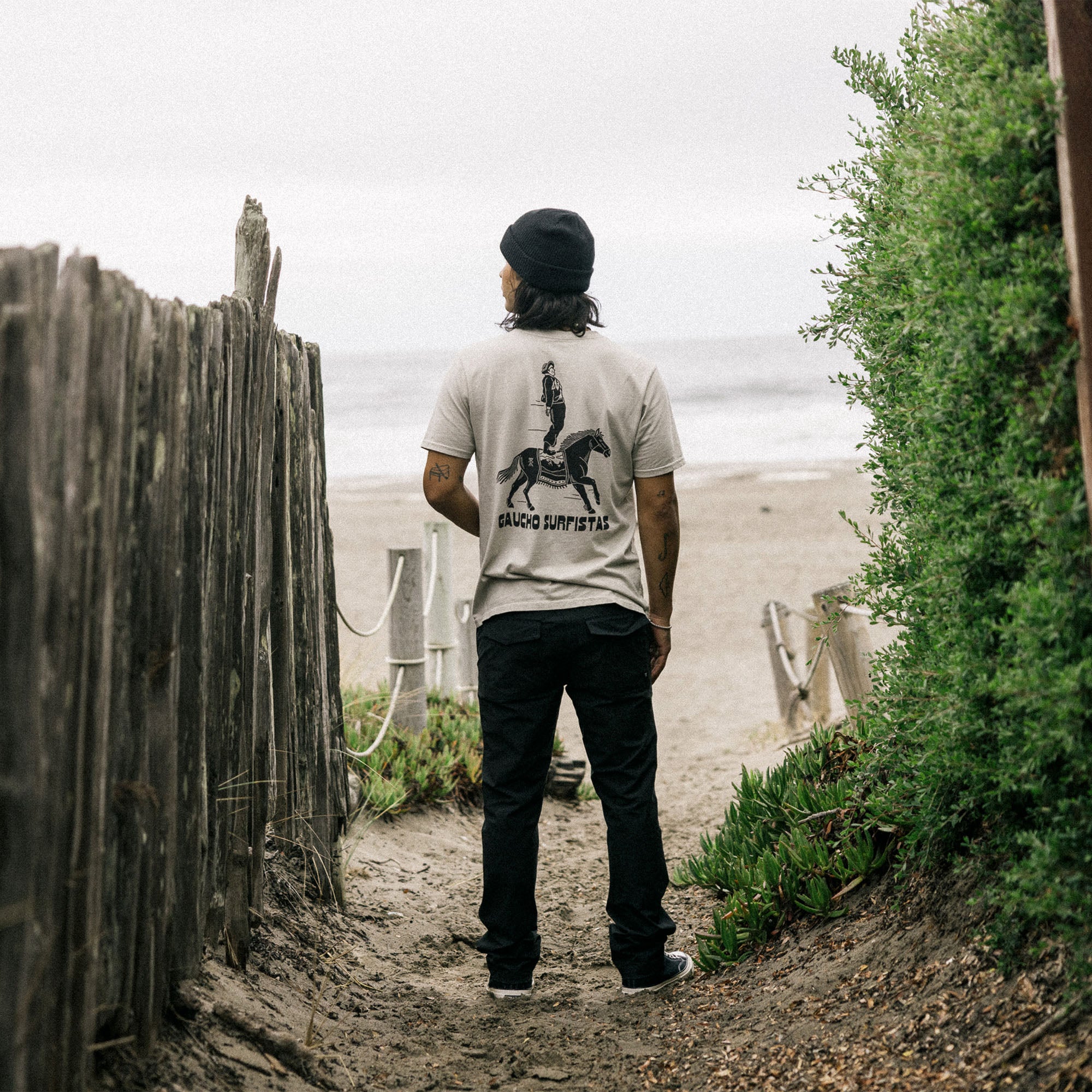 Scenic coastal view depicted on the Tierra del Sur Surfista Premium Tee, capturing the essence of adventure with a stunning beach, sea, and ocean backdrop.