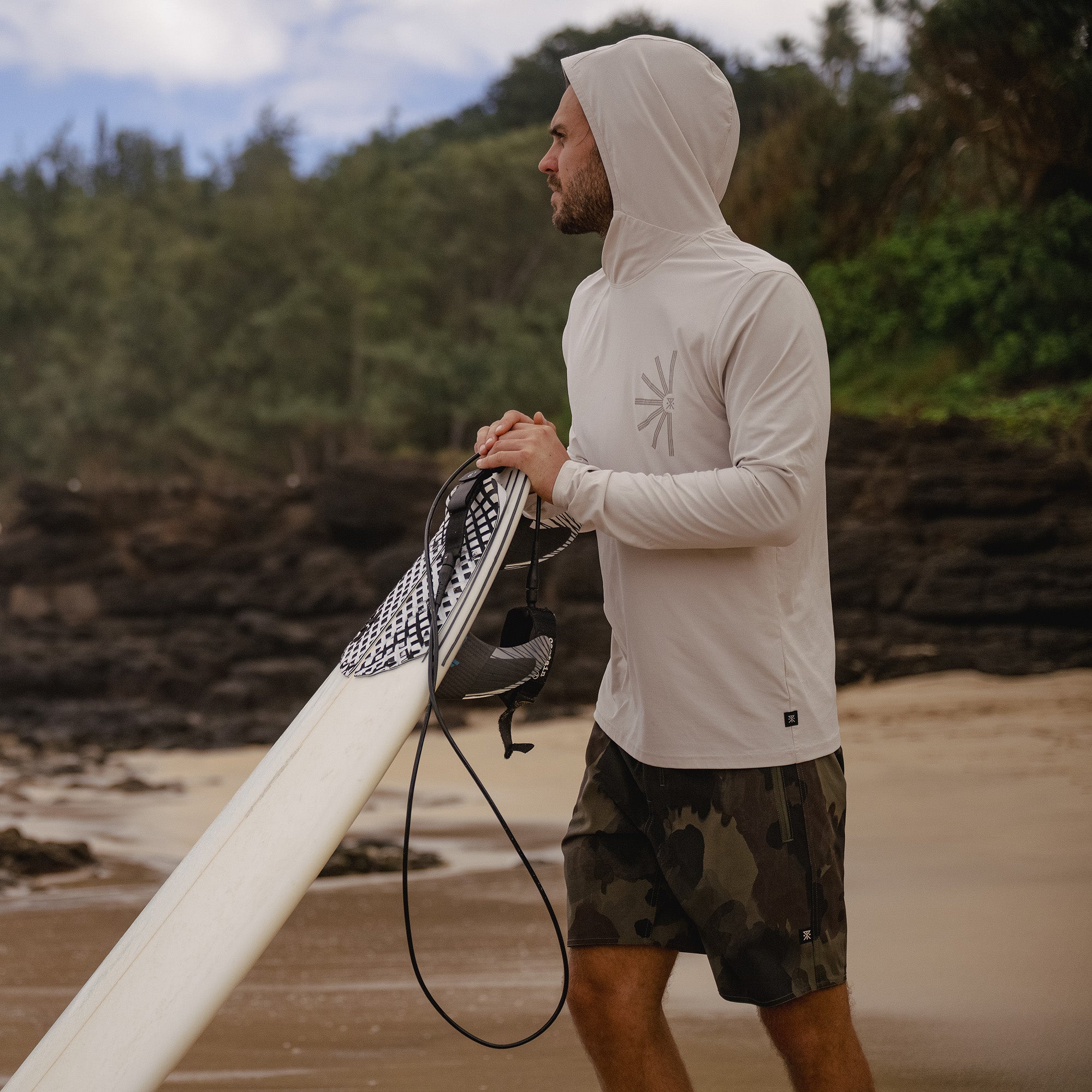 Surfer wearing a UPF hoodie while carrying a surfboard, preparing to enter the ocean for a water sports adventure