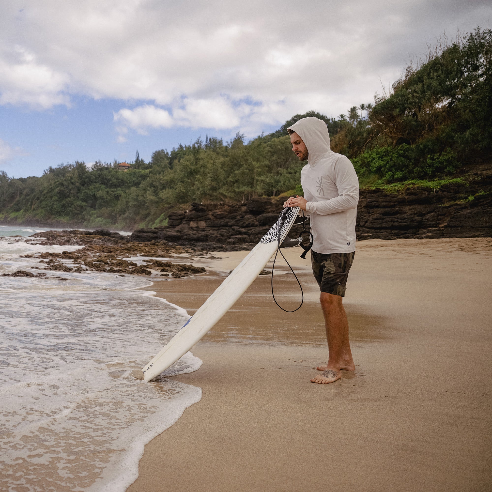 Surfer wearing a Venture UPF hoodie paddling out on a surfboard in the ocean, ready for a day of water sports.