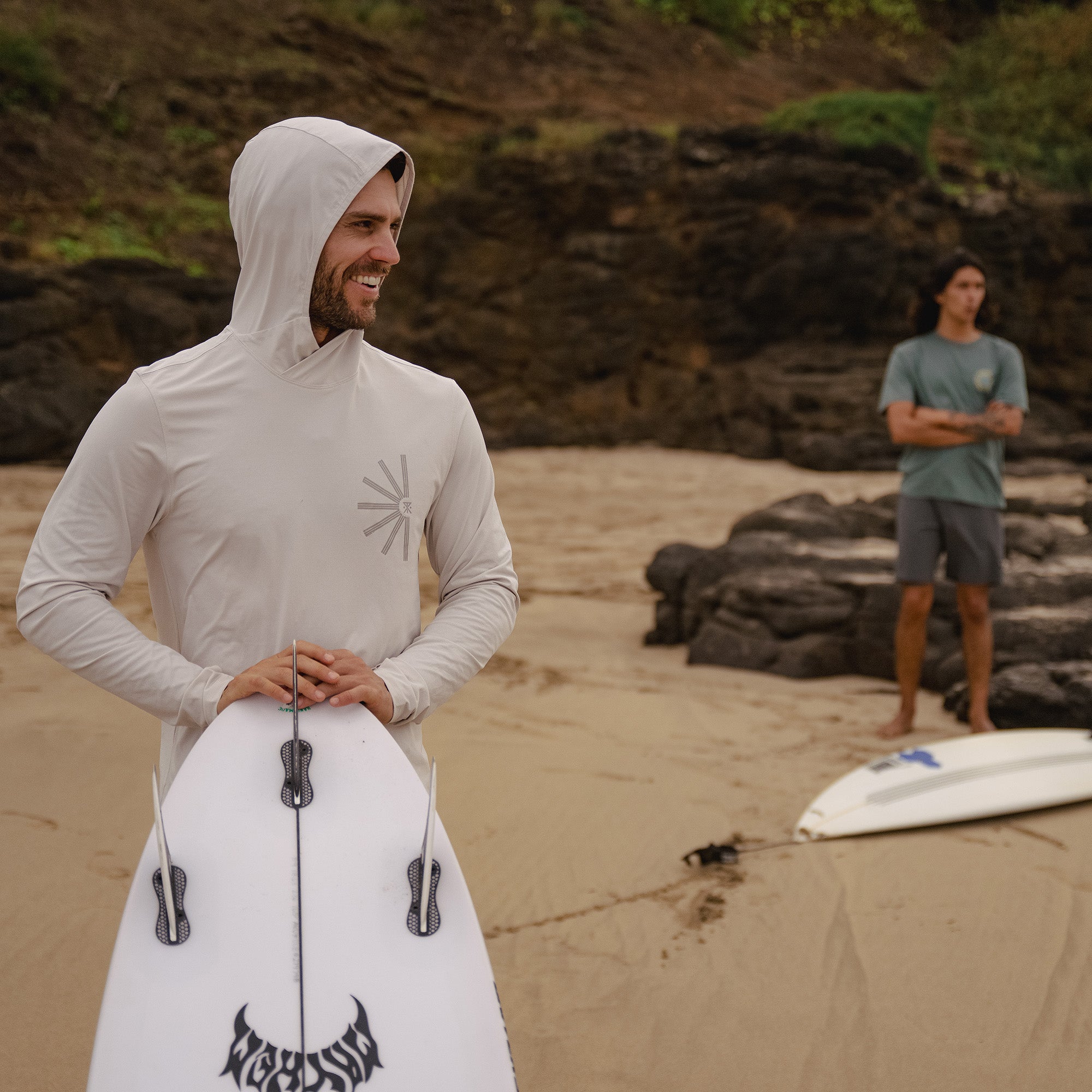 Surfer wearing Roark's Venture UPF Hoodie while carrying a surfboard along the beach, highlighting the hoodie's suitability for water sports and outdoor adventures.