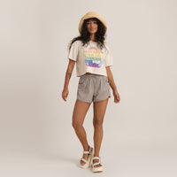 Casual summer outfit with graphic tee, grey shorts, straw hat, and white sandals on a woman.