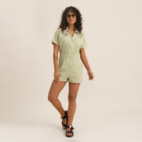 Fashion-forward woman in a light green romper with embroidery, paired with sunglasses and navy sandals.
