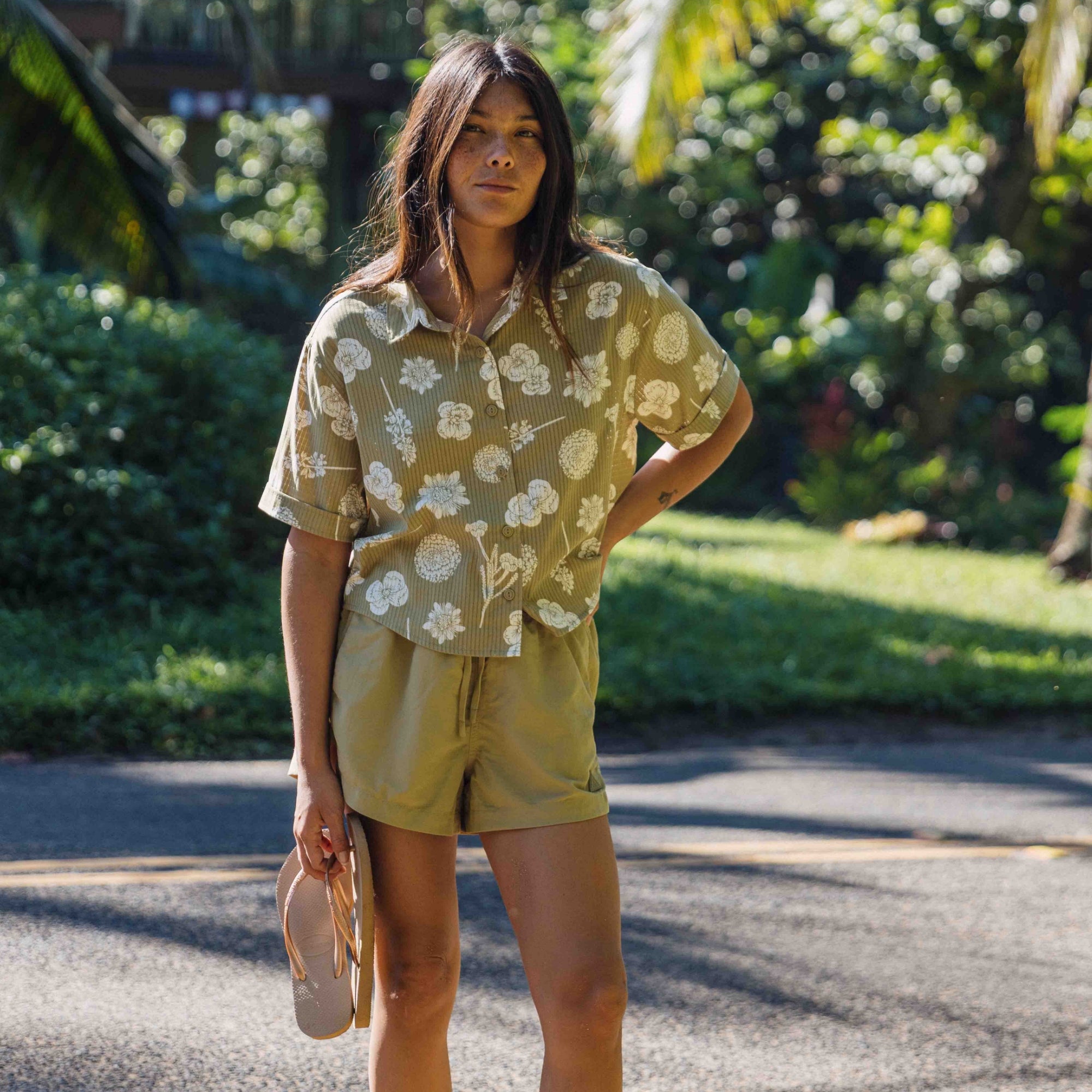 Woman wearing the Roark Bless Up casual shirt, stylishly tied at the waist and paired with knee-length shorts, perfect for travel and outdoor adventures.