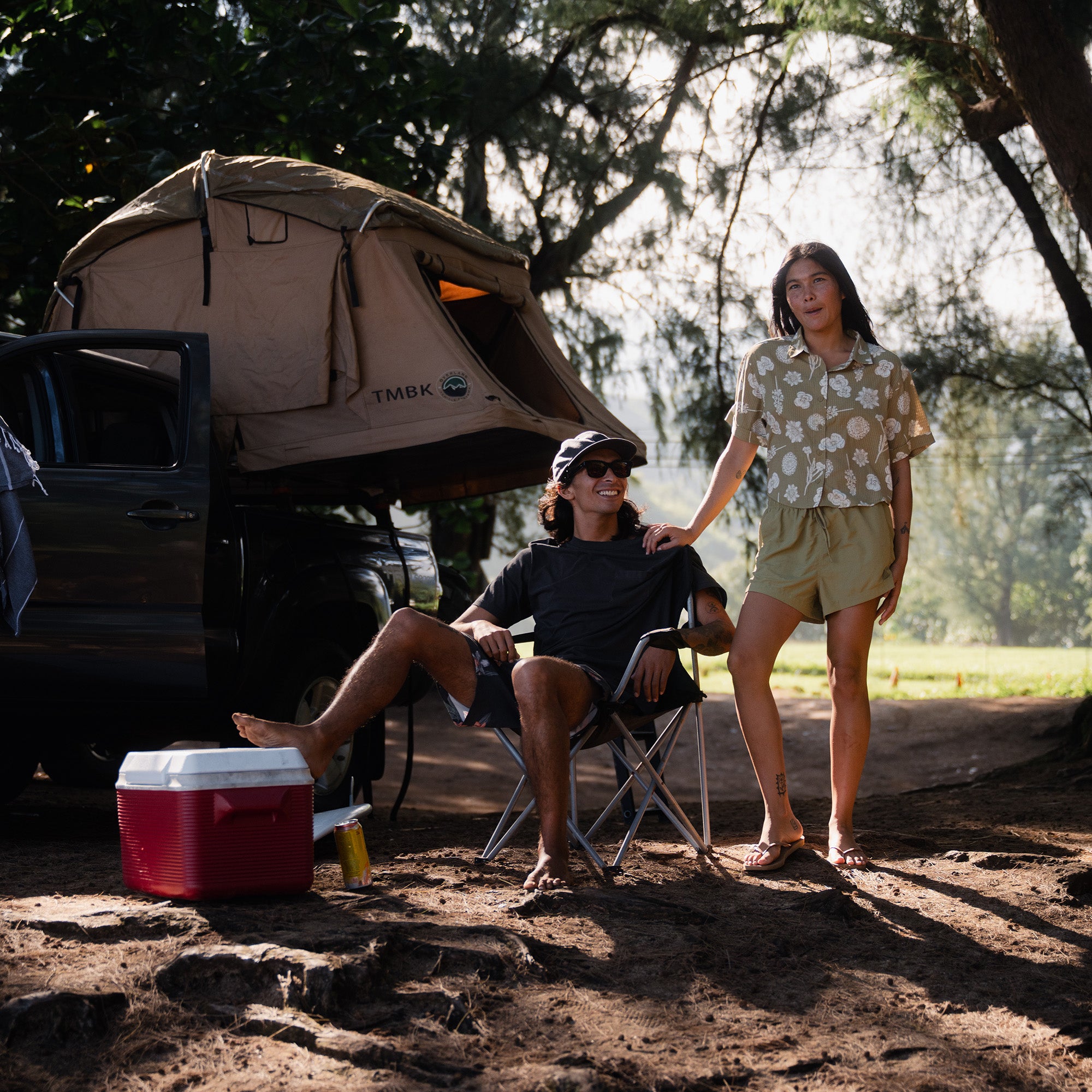 Adventure-seeking woman relaxing by her tent at a scenic campsite, embodying the spirit of travel and recreation, wearing Roark's outdoor apparel.