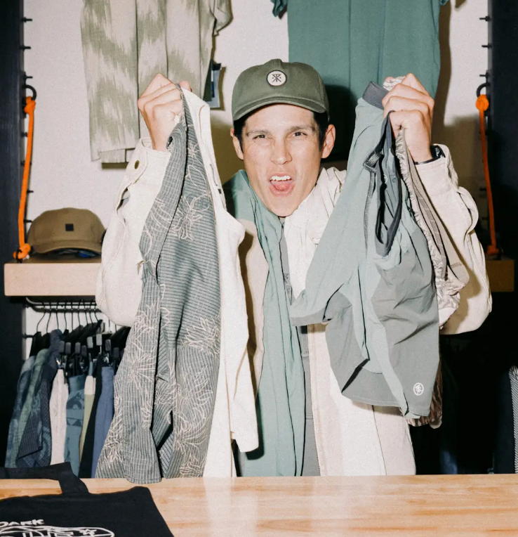 Shopper examining a display of baseball caps and outdoor travel gear at Roark retail store.